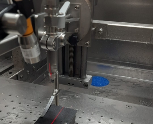Druckwasserstrahlprüfung in der DWT: Düse über dem Probentisch, ein Positionierlaser markiert den Auftreffpunkt