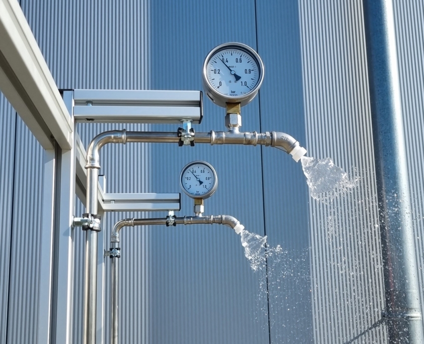 Rain Test nach UL 50E: zwei Sprühköpfe in Betrieb, das Manometer zeigt rund 0,35 bar (5 psi)